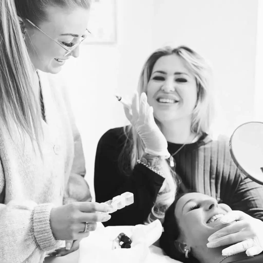 Drei Frauen lächeln und lachen zusammen während eines kosmetischen Eingriffs, eine hält eine Spritze.